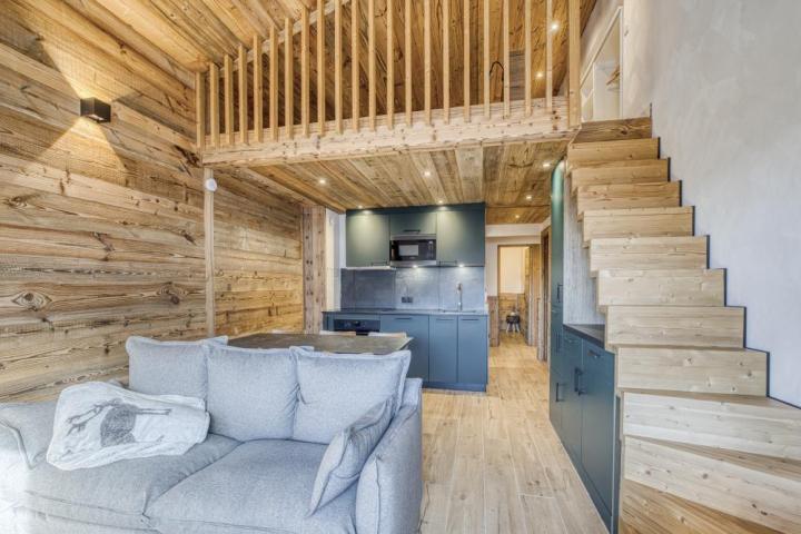 Réalisation en vieux bois ! Alpine Habitat & Studio Veyrat. Crédit photo : Lilian Chapel photographe  Rénovation intérieure d'un chalet en vieux bois à l'atmosphère authentique et chaleureuse. Studio salon / cuisine avec un canapé gris et des façades de mobiliers bleu-vert. Habillage mural, escalier, mezzanine en vieux bois.