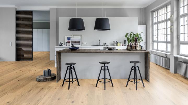 Quel parquet choisir ? Le guide complet. Parquet contrecollé dans une cuisine. 3 tabourets sont devant le plan de travail.