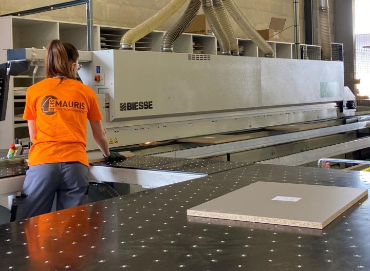 service découpe Mauris Bois, un atelier pour vos projets sur mesure machine à commande numérique qui façonne un panneau. Employée Mauris Bois au commande avec un tee-shirt orange.