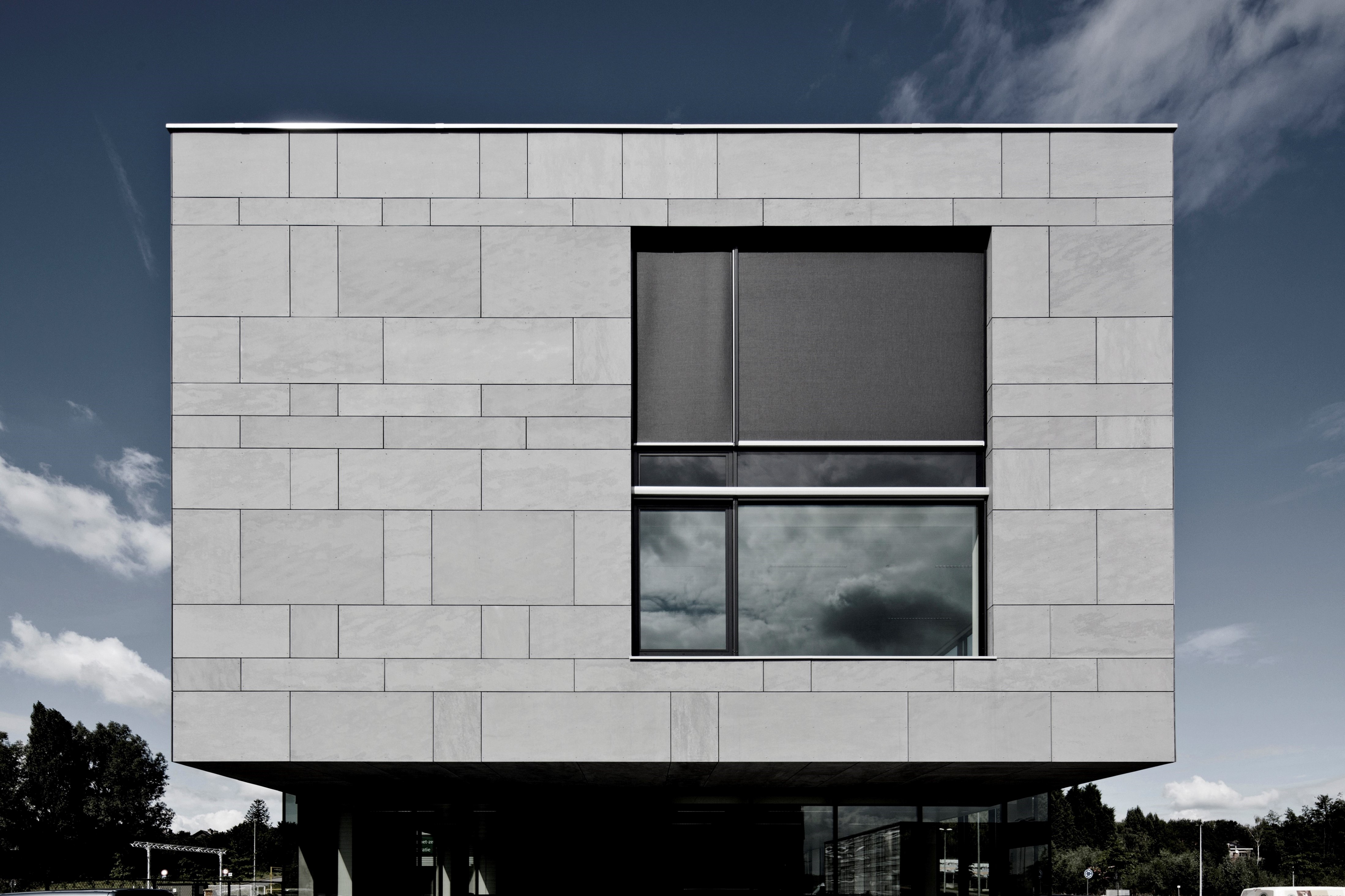 Panneaux de façade Equitone Tectiva. Photo de réalisation. Façade d'un bâtiment avec des panneaux gris et une grande fenêtre sur la droite du bâtiment.